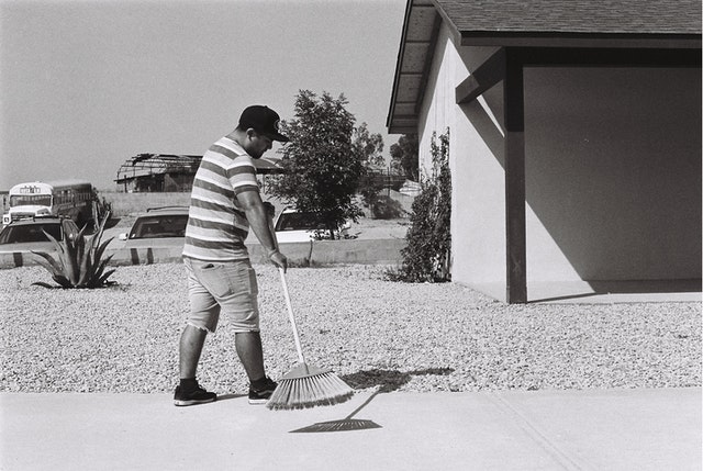grayscale-photo-of-man-sweeping-driveway-2305091